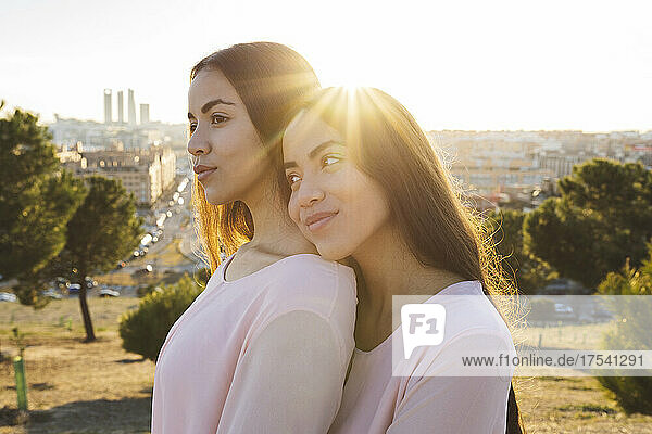 Smiling woman embracing thoughtful sister at sunset