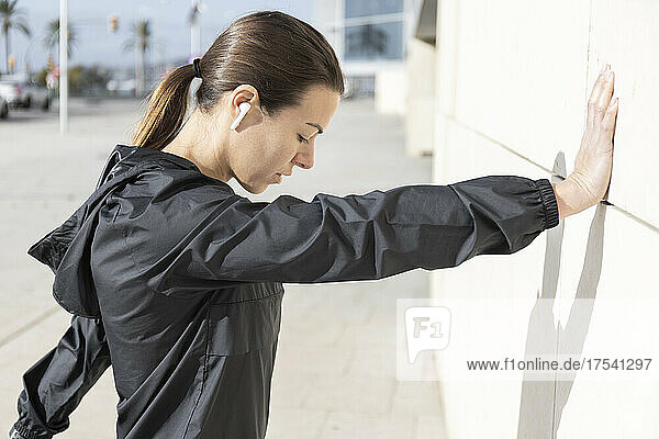Athletic woman doing warm up exercise leaning on wall