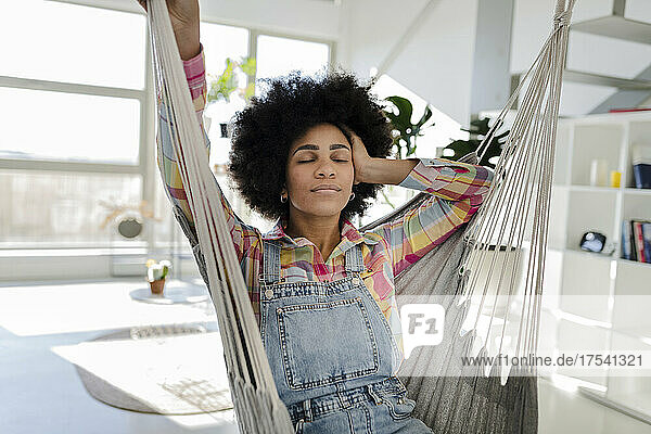 Young woman with closed eyes relaxing in swing at home