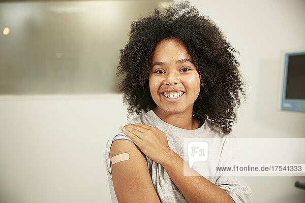 Smiling girl with curly hair showing vaccinated arm in hospital room