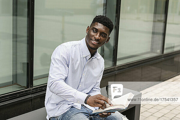 Smiling young man with book sitting on bench