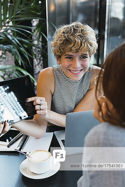 Smiling freelancer showing tablet PC to colleague in cafe