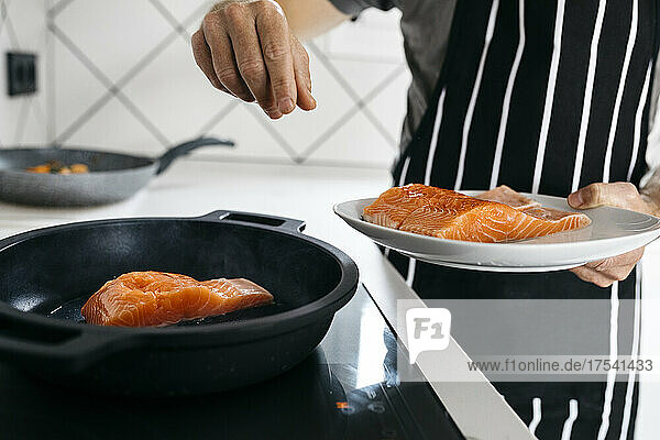 Man preparing fish in cooking pan at home