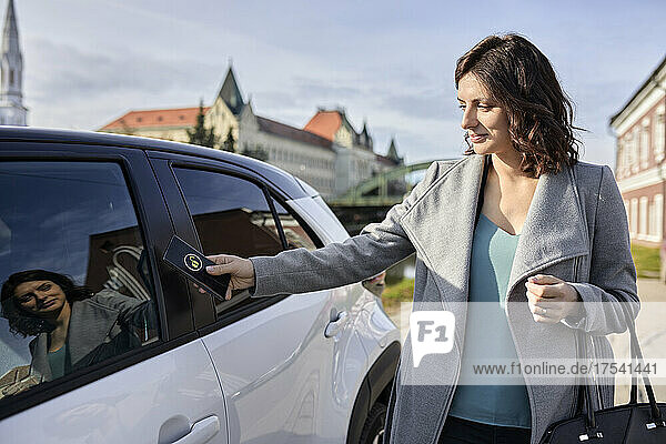 Woman unlocking electric car through smart phone on sunny day