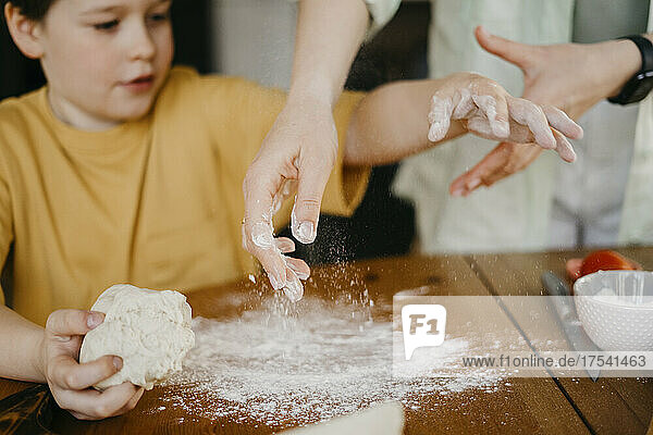 Mother helping son to knead dough on table