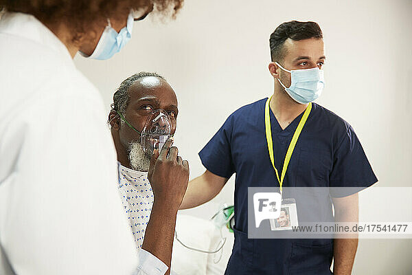 Patient adjusting oxygen mask looking at doctor in medical room