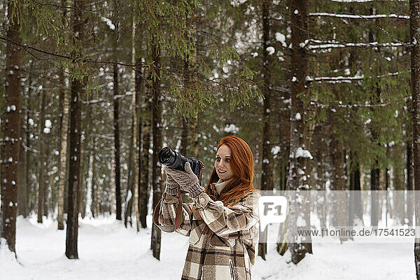 Redhead woman photographing through camera in winter forest