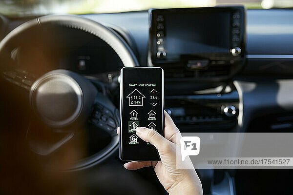 Businesswoman controlling smart house through mobile phone in car