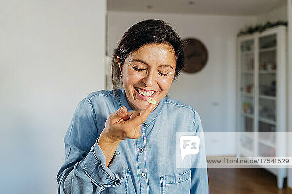 Cheerful woman tasting food with finger at home