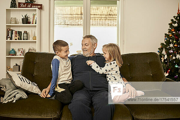 Boy and girl sitting with grandfather on sofa at home