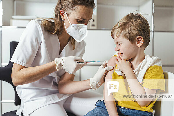 Boy closing eyes and getting vaccinated by nurse at center