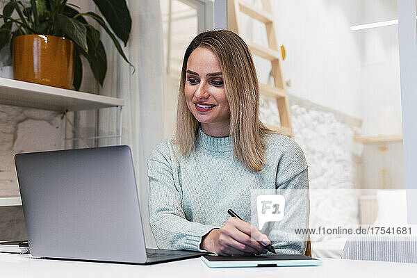 Businesswoman using graphic tablet looking at laptop in studio