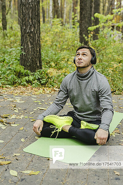 Young man with headphones sitting cross-legged on exercise mat at park