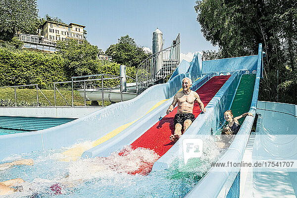 Grandfather and grandchildren enjoying water slide in swimming pool