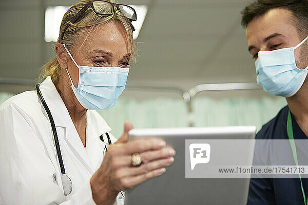 Healthcare workers with protective face mask sharing tablet PC in medical room