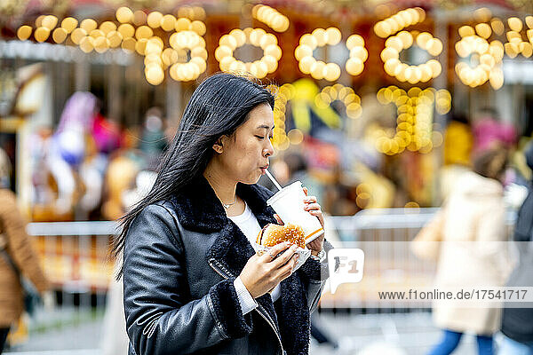 Woman holding burger and drinking from disposable cup at park