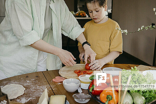 Woman teaching boy cutting tomato at home