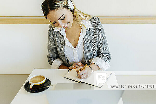 Young freelancer with coffee cup writing in diary on table