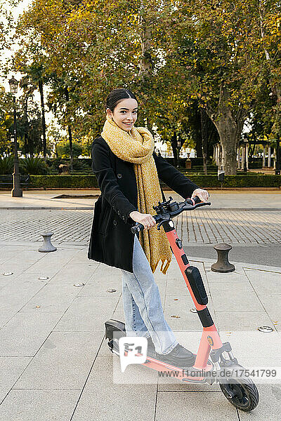 Smiling teenage girl riding electric push scooter on footpath