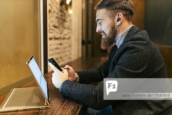 Smiling businessman using mobile phone and listening music through in-ear headphones