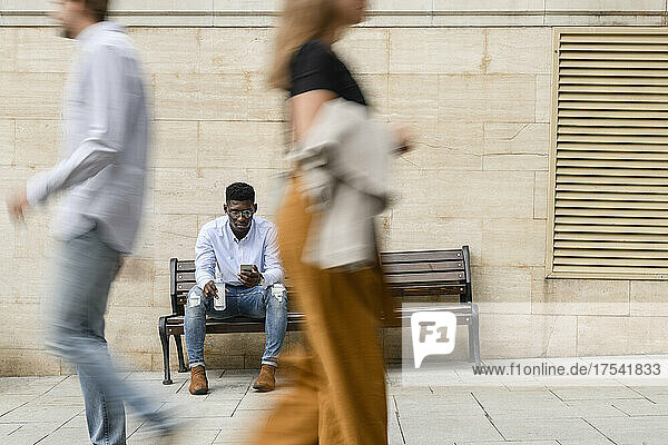 Young man with water bottle using smart phone on bench