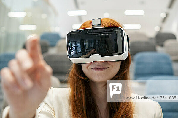 Smiling businesswoman wearing virtual reality headset gesturing in office