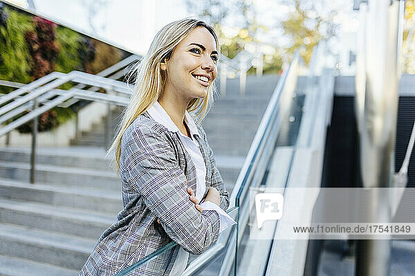 Smiling blond businesswoman leaning on staircase railing