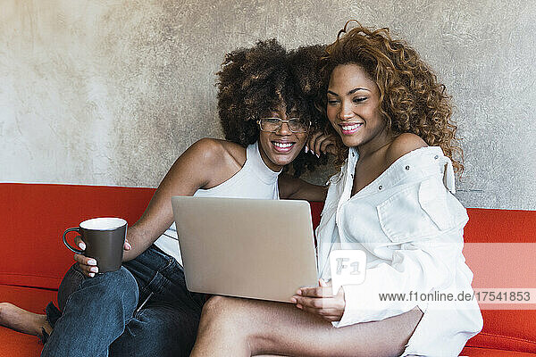 Woman using laptop with friend on sofa