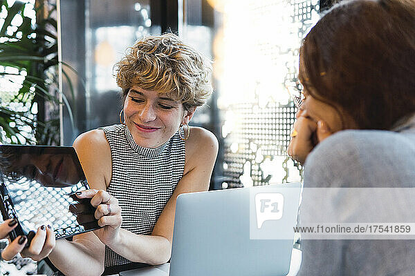 Smiling businesswoman showing tablet PC to colleague at coffee shop