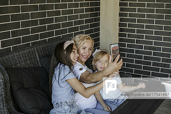 Lächelnde Großmutter macht Selfie mit Enkelinnen auf dem Smartphone