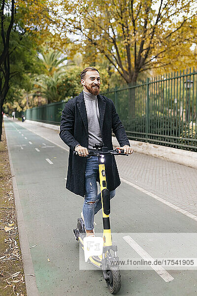 Glücklicher Mann fährt Elektroroller auf Fahrradweg