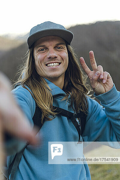 Happy man taking selfie and making peace sign on mountain