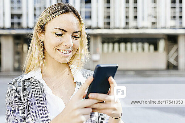 Smiling young blond businesswoman using smart phone