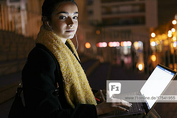 Teenage girl with laptop listening music on headphones at night