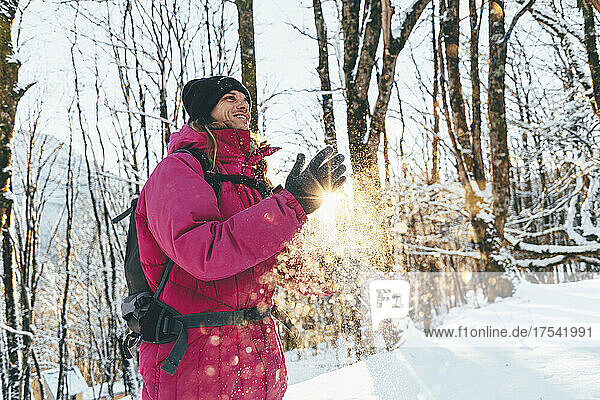 Smiling tourist dusting snow from hands in forest