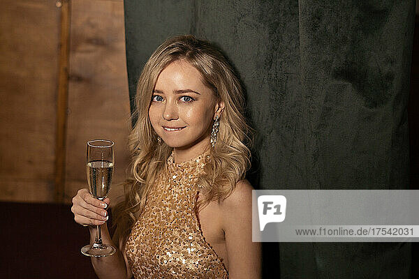 Beautiful woman holding champagne flute by black curtain