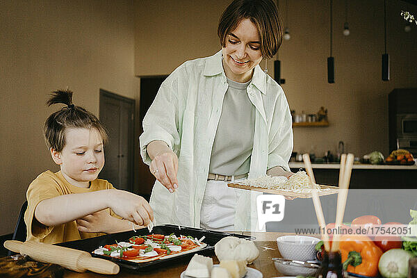 Mother and son adding cheese on pizza at home