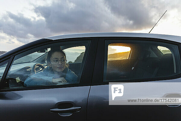 Junge Frau blickt bei Sonnenuntergang durch das Autofenster