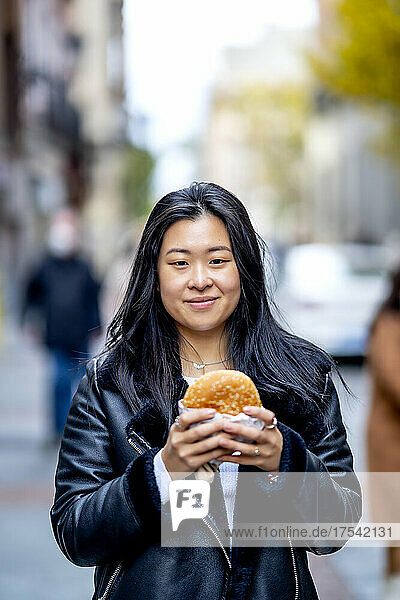 Smiling young woman with long black hair holding burger