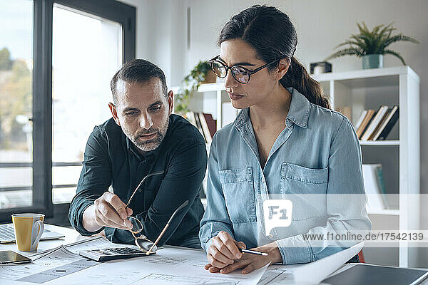 Businessman discussing over blueprint with colleague in small office
