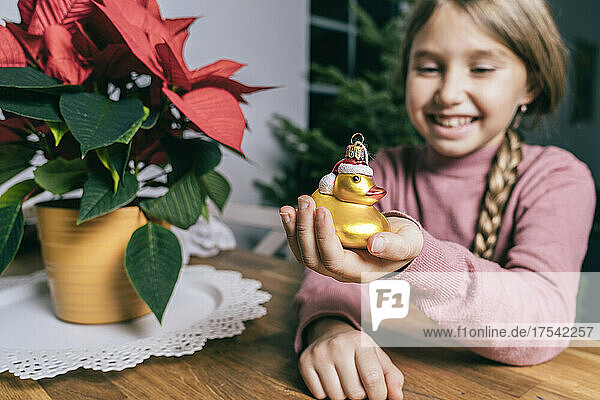 Smiling girl holding golden Christmas duck by star plant at home
