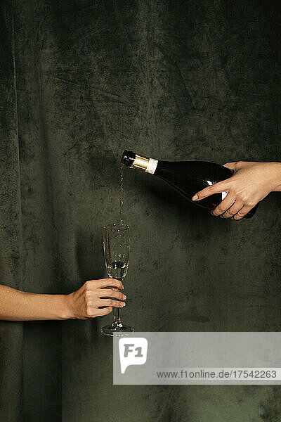 Hand pouring champagne in flute held by woman in front of black curtain