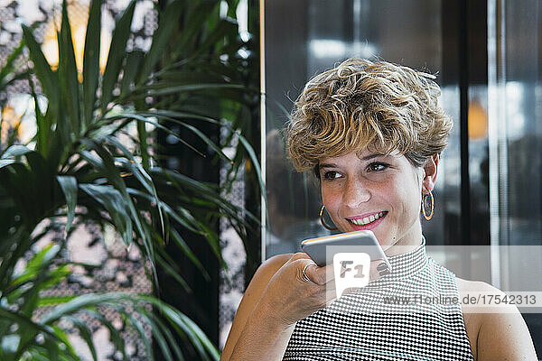 Smiling businesswoman sending voicemail on smart phone at coffee shop