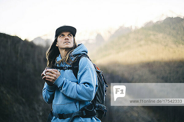 Backpacker holding coffee mug contemplating on mountain