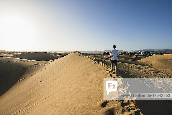 Young man walking on sand under clear blue sky at sunset  Grand Canary  Canary Islands  Spain
