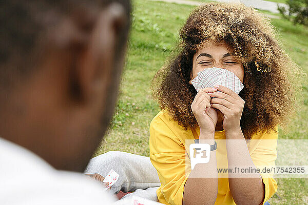 Cheerful woman playing cards with friend in park