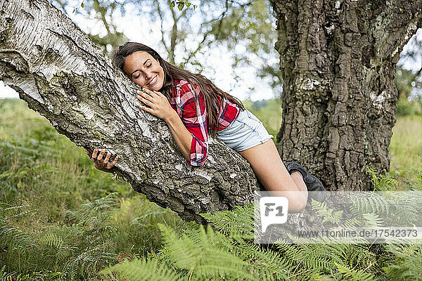 Smiling woman relaxing on tree branch in forest at Cannock Chase