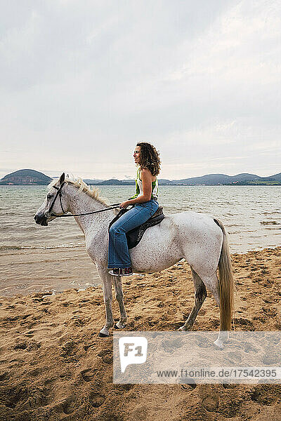 Smiling young woman riding horse at waterfront