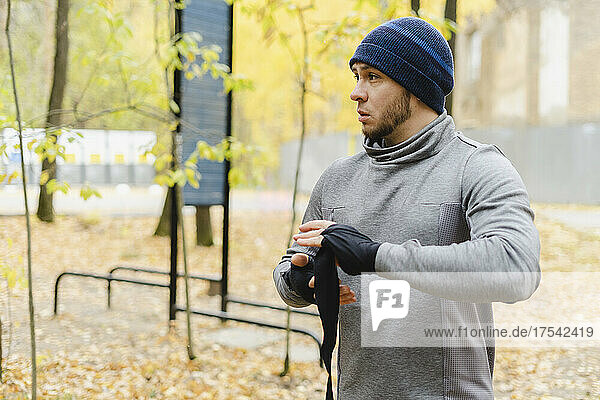 Young man with knit hat wrapping bandage on hand at park