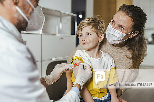 Doctor putting bandage on smiling boy's arm at center